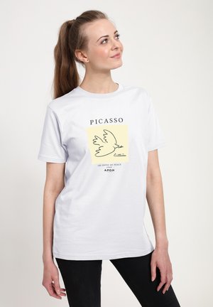 Bílé bavlněné tričko s černým liniovým obrázkem holubice na žlutém pozadí, s nápisem „PICASSO“ nahoře a textem dole.