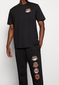 Czarny bawełniany t-shirt z krótkim rękawem i okrągłym dekoltem, z kolorową grafiką na piersi. Czarne spodnie dresowe z wyszywanymi naszywkami.