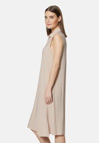 Lässiges, ärmelloses Kleid aus leichtem beigen Stoff. Besitzt einen subtilen Glanz und endet knapp über dem Knie, was eine lockere Silhouette bietet.
