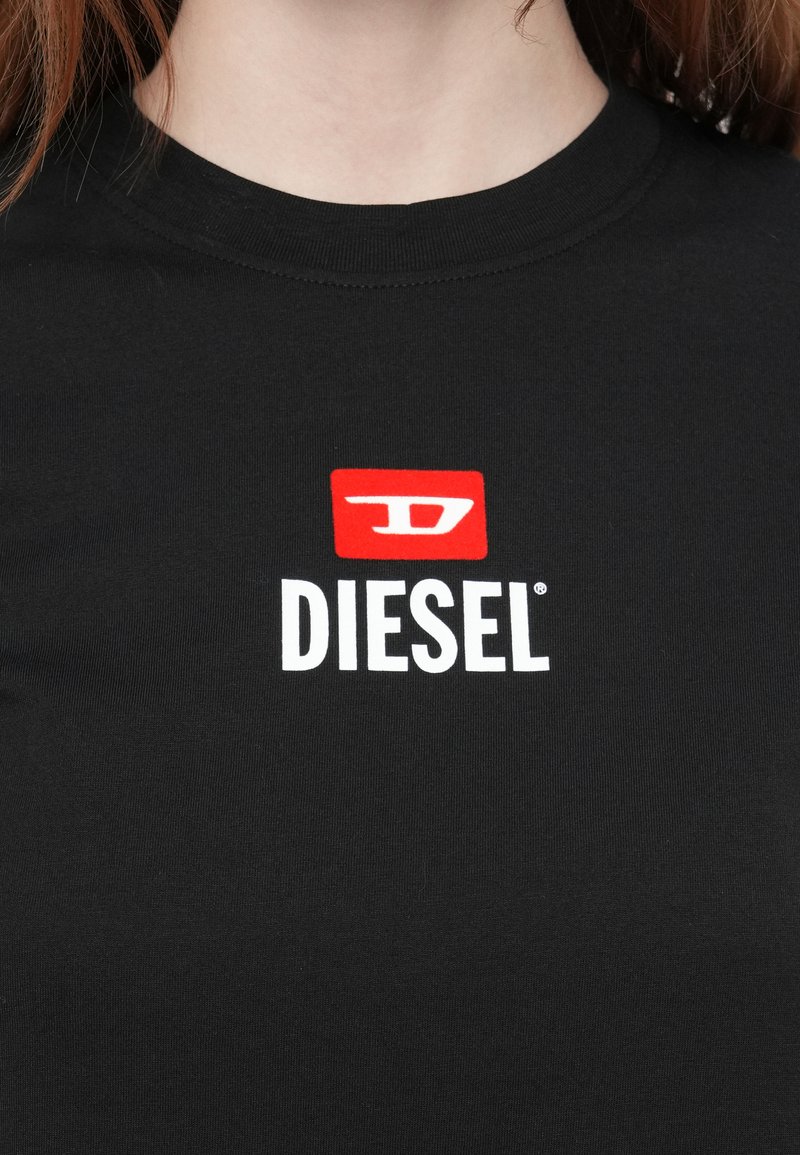 Maglietta nera a girocollo con un logo Diesel bianco e rosso centrato sul petto, indossata da una persona con pelle chiara e capelli castani.