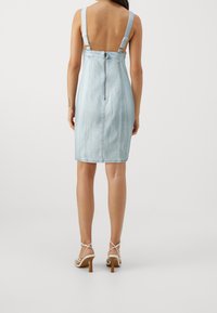 Vaaleansininen farkumekko, jossa on istuva siluetti, leveät henkät ja takavetoketju. Sujuva pinta ja polvipituinen muotoilu.