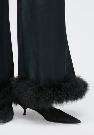 Crne hlače širokih nogavica od baršuna s pufastim crnim krznom na rubu, uparene s crnim štiklama s špicastim vrhom. Meka tekstura, elegantan dizajn.