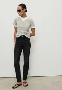 Light gray V-neck t-shirt with white trim, paired with black straight-leg jeans and black flip-flops with studded accents.
