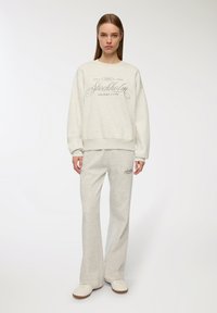 Set di felpa e pantaloni della tuta grigio chiaro. La felpa presenta un collo rotondo e un logo stampato "Stockholm Leisure Club". Tessuto morbido.