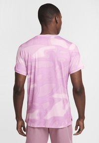 Camiseta atlética de manga corta en rosa claro con un patrón ondulado, hecha de tela transpirable, que presenta un ligero ajuste en el dobladillo.