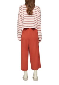 Skrócony sweter w paski w kolorze różowym i białym, zestawiony z pomarańczowymi spodniami o szerokich nogawkach. Teksturowana tkanina, luźny krój i casualowy design.