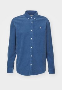 Camisa de pana azul de manga larga con cuello abotonado, botones blancos y pequeño logo bordado en el pecho. Tejido texturizado.