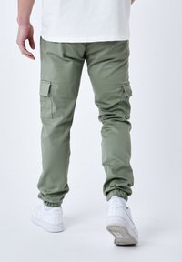 Lysgrønne cargo-bukser med elastiske manchetter, sidelommer og en glat stoftekstur, parret med hvide sneakers.