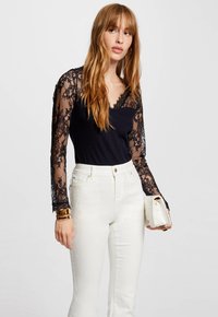Bodysuit noir avec des manches longues en dentelle, présentant un décolleté en V ; associé à un jean blanc taille haute et un petit sac à main blanc.