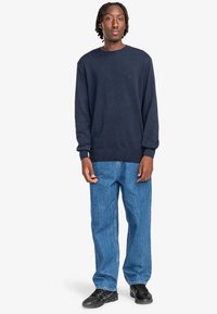 Marineblauer Pullover aus weichem Material mit Rundhalsausschnitt, kombiniert mit hellblauen geraden Jeans und schwarzen Sneakers. Einfaches Design, keine Muster.