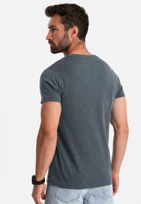 Tmavě šedé tričko s krátkým rukávem a kulatým výstřihem, vyrobené z měkké tkaniny, přiléhavého střihu a jednofázové textury. Obsahuje minimální detaily šití.