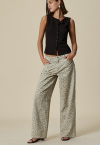 Haut sans manches noir texturé avec des boutons à l'avant, associé à un pantalon large vert clair arborant un motif léopard subtil.