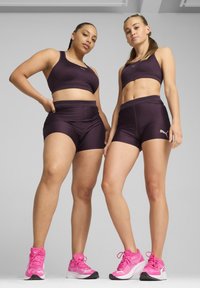 Lilla atletiske crop tops og shorts lavet af glat stof, parret med lyserøde løbesko med teksturerede detaljer og snørebånd.