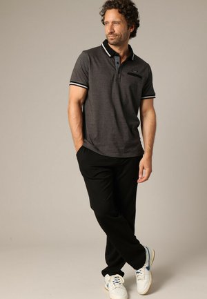 Polo shirt charbon avec un col noir et des rayures blanches, comportant une poche. Associé à un pantalon noir et des baskets blanches.