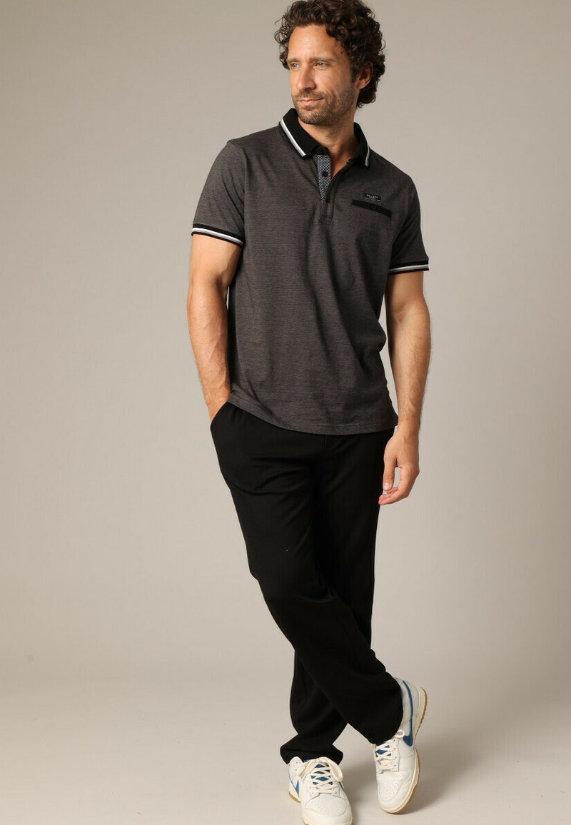 Polo shirt charbon avec un col noir et des rayures blanches, comportant une poche. Associé à un pantalon noir et des baskets blanches.