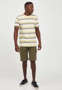 T-shirt à rayures à manches courtes en jaune, gris et blanc avec un col rond ; assorti à un short cargo vert olive et des baskets noires.