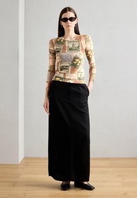 Long-sleeve top with a multi-pattern print in beige, paired with a black, floor-length skirt and flat black shoes.