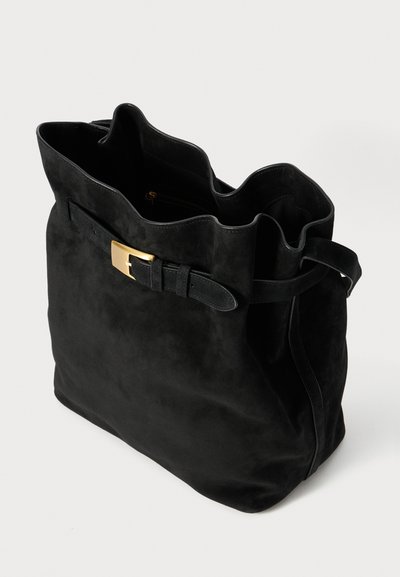Black suede tote bag with a wavy top edge, gold hardware buckle detail, and a single adjustable strap. Interior zip pocket visible.