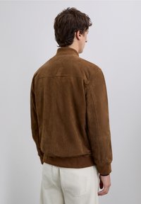 Brown suede bomber jacket with a stand collar, ribbed cuffs, and hem. Seam detailing along the back, smooth texture.