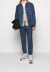 Chaqueta de denim de color azul claro, con dos bolsillos en el pecho, combinada con una camisa beige y jeans azules a juego, complementada con zapatillas blancas y negras.