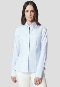 Jasnoniebieska, długorękawowa koszula zapinana na guziki, wykonana z gładkiego materiału, o dopasowanym kroju z bocznymi szwami, klasycznym kołnierzykiem i zapięciem na guziki.