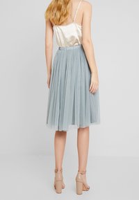Gonna in tulle azzurro chiaro con design plissettato, caratterizzata da una vita alta e una cintura elastica. Indossata con sandali nudi con tacco a blocco.