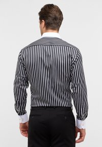 Camicia a righe bianco e nero con colletto classico e polsini bianchi a contrasto. Presenta maniche lunghe e un design della schiena dritto.