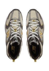 Zapatillas de running grises y amarillas con parte superior de malla y patrón hexagonal, cordones blancos y logotipo destacado en la lengüeta. Suela de goma gruesa.