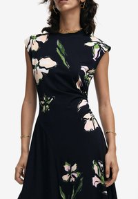 Schwarzes Kleid mit kurzen Ärmeln, verziert mit großen rosa und grünen Blumenmustern. Glatter Stoff mit taillierter Passform, an der Taille betont.