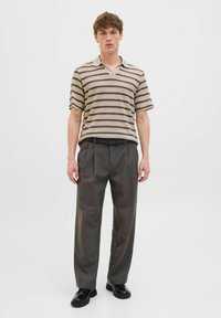 Polo cu dungi în nuanțe de bej și maro, asortat cu pantaloni cu talie înaltă de culoare gri închis. Outfitul are mâneci scurte și o croială lejeră.