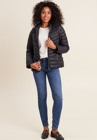 Giubbotto piumino imbottito nero con cappuccio, zip frontale e tasche laterali. Abbinato a jeans skinny blu chiaro e mocassini neri.