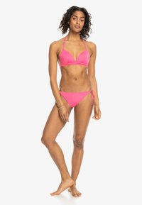 Růžový bikini s trojúhelníkovým vrškem a nastavitelním zavazováním na bocích, vyrobený z hladkého, elastického materiálu.