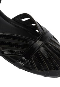 Schwarze Lackleder-Sandale mit diagonalen Ausschnitten, kreuzenden Riemen und kontrastierenden Nähten. Elegantes Design mit glatter Textur.