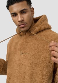 Brown fleece hoodie with a textured surface, front drawstring closure, and a small embroidered logo in gold.