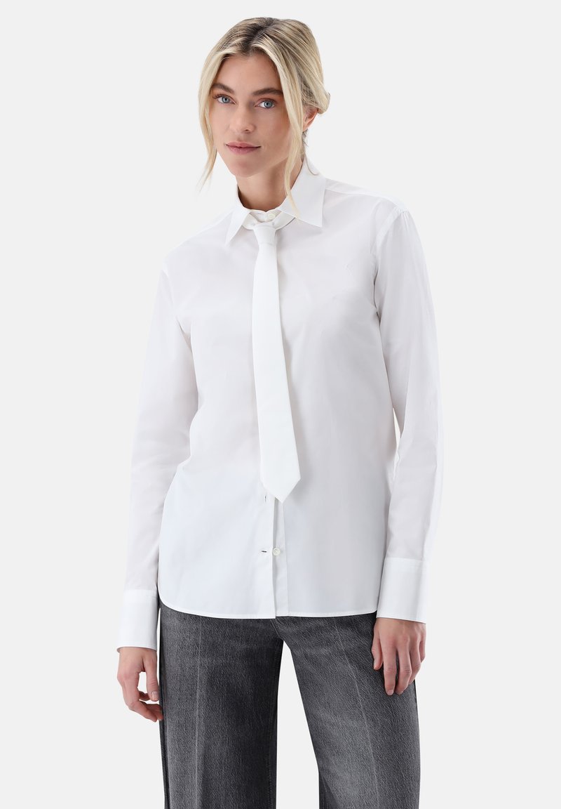 Camicia bianca con bottoni, collo rigido e cravatta annodata, realizzata in tessuto liscio. Presenta maniche lunghe e taglio dritto. Abbinata a pantaloni grigi.