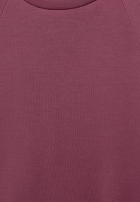 Nahaufnahme eines schlichten, mauvefarbenen, ärmellosen Oberteils, das die Stoffstruktur sowie die genähte Hals- und Schulternaht zeigt.