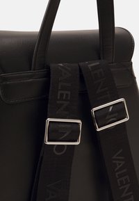 Černá kožená taška s výrazným designem, vybavená dvěma černými popruhy se stříbrným kováním a vyraženými detaily loga.