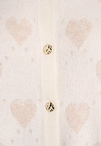 Balts kardigans ar maigiem bēša sirds rakstiem, trīs pogām ar raibumu un ribota apkakli un apakšu.