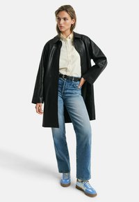 Black leather coat with a collared design, paired with a light button-up shirt, blue jeans, and blue-accented sneakers.