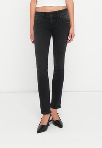 Jeans neri skinny con un design aderente, stile a cinque tasche e una leggera lucentezza. Abbinati a tacchi neri a punta.