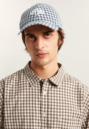 Blauw-wit geruite pet met een gebogen rand en geborduurd "VANS" logo; model draagt een bruin-wit geruit overhemd met knopen.