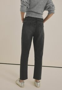 Sorte højtaljede jeans har en lige pasform, baglommer og frynsede kanter. De er parret med sølvfarvede sneakers og en struktureret grå sweater.
