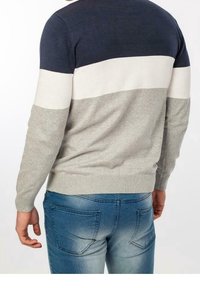 Pull léger bleu marine, blanc et gris. Caractéristiques : col rond et poignets côtelés. Associé à un jean en denim bleu avec poches à l'arrière.