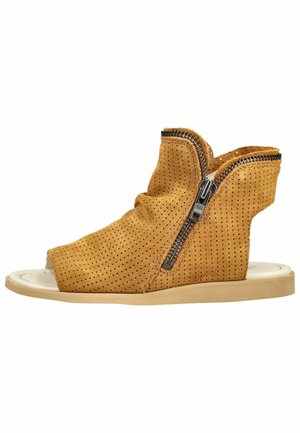 Beżowy, perforowany sandał na koturnie z zamkiem błyskawicznym po boku i odkrytymi palcami, płaską podeszwą i wysokim zakryciem kostki.