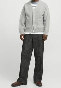 Grå stickad cardigan med v-ringning, två framfickor och knappar, lager på lager över en randig skjorta och matchad med mörka vida jeans.