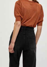 Rostfärgad kortärmad stickad topp med texturerad yta, matchad med högmidjade svarta denimjeans med bakfickor.