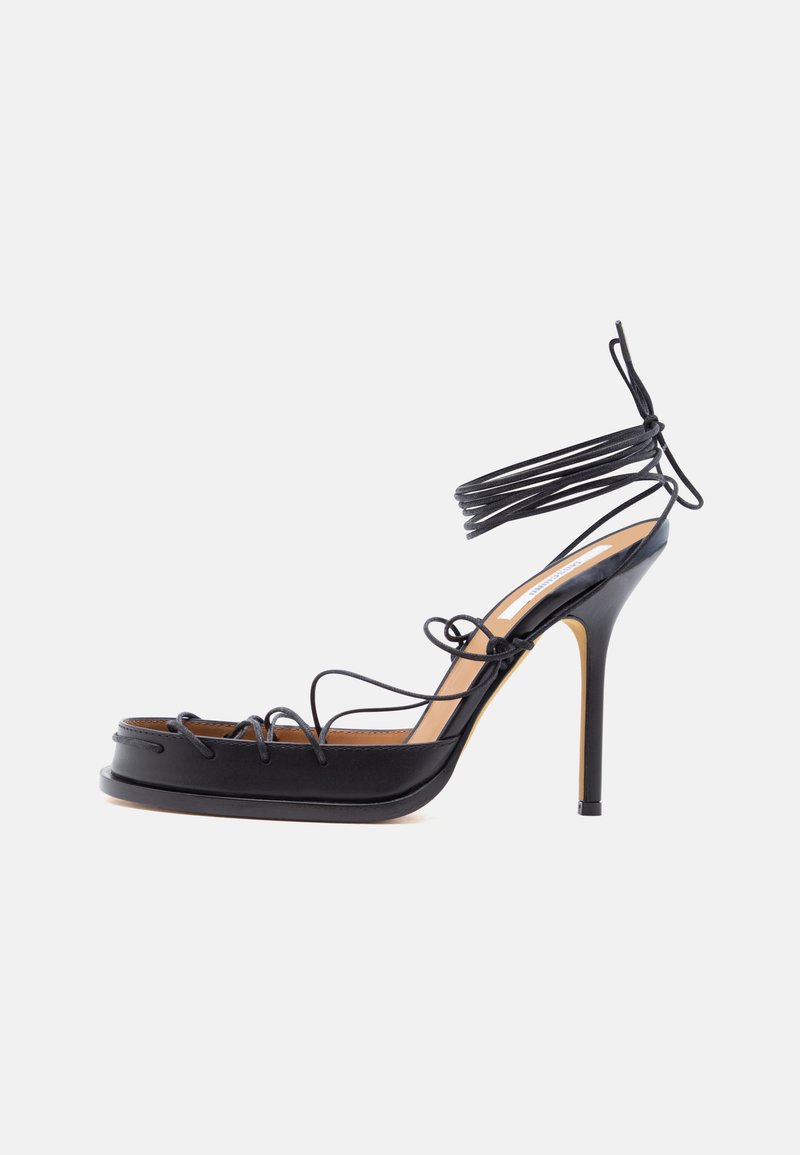 Μαύρο ψηλοτάκουνο σανδάλι με λεπτά δερμάτινα λουράκια που τυλίγονται γύρω από το πόδι και τον αστράγαλο, με αιχμηρή στιλέτο φτέρνα.