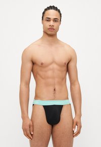 Crne tange s elastičnom trakom svijetloplave boje na kojoj je oznaka "Calvin Klein", izrađene od mekanog materijala za udobnost.