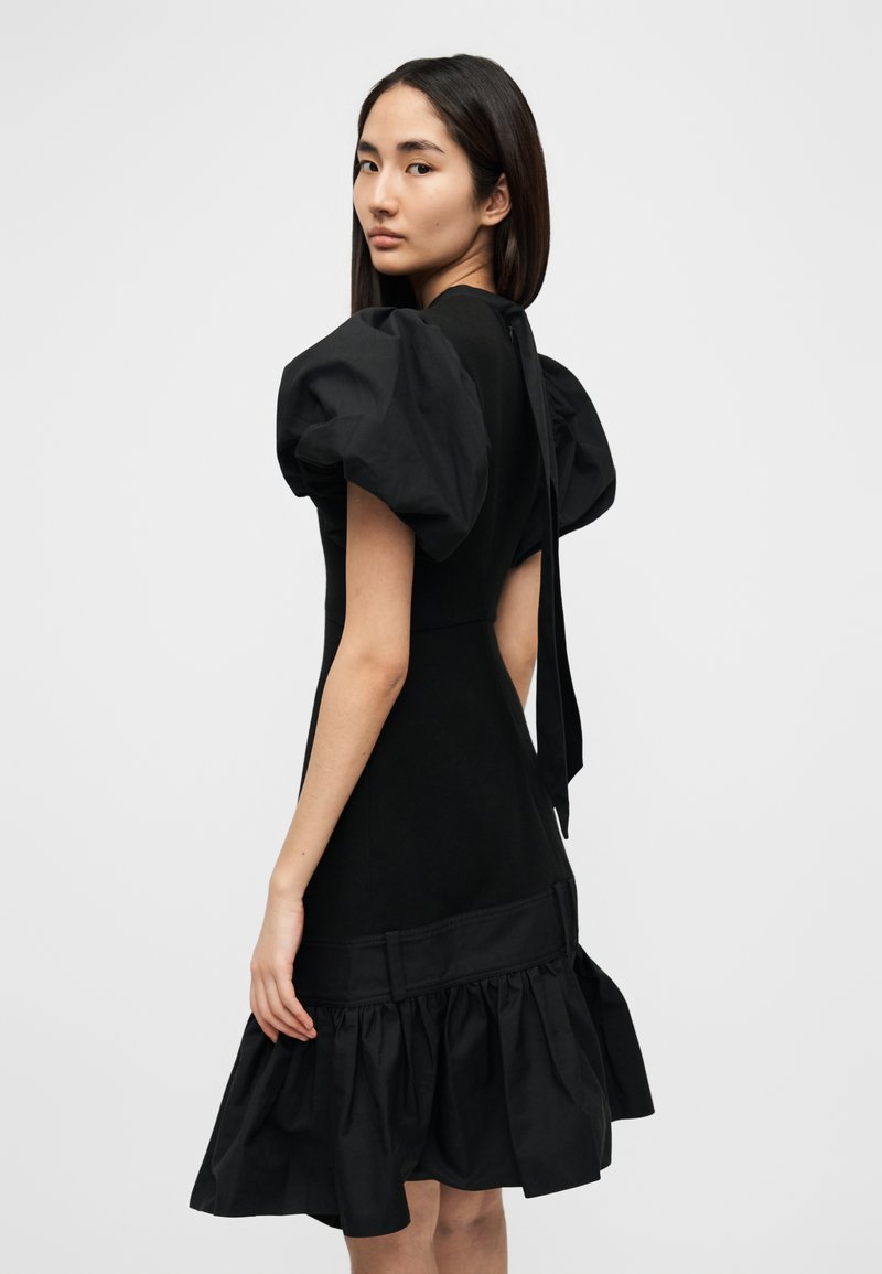 Vestito nero in cotone con maniche a sbuffo e orlo svasato arricciato. Presenta un corpetto aderente e una cintura larga in vita.