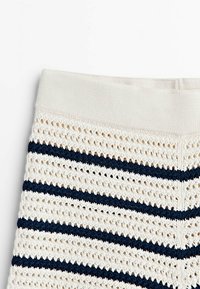 Tissu crocheté à rayures crème et bleu marine avec une ceinture élastique unie crème, montrant une texture tricotée et un motif ajouré.